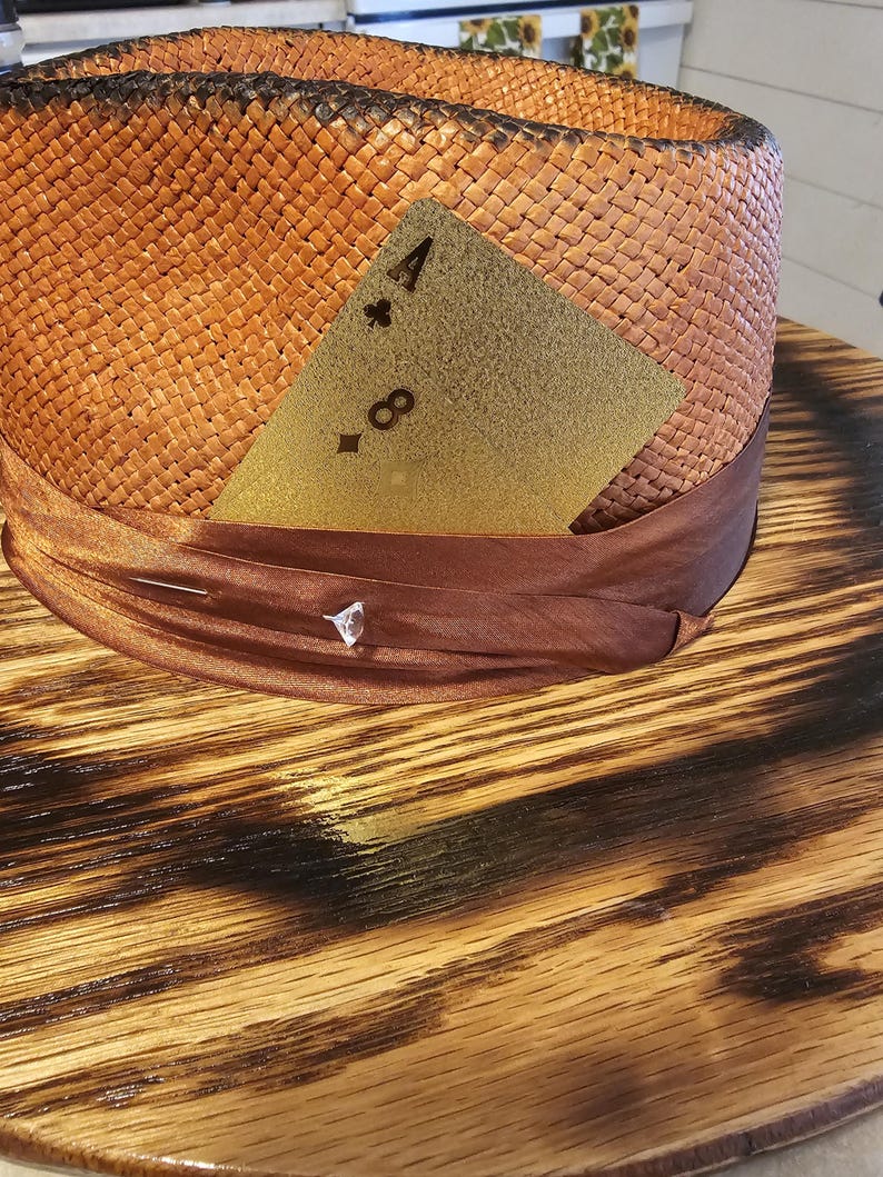 May include: A brown woven straw hat with a brown ribbon and a gold playing card with the number 4 of clubs on it.