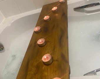 Puede incluir: Una bandeja de baño de madera con seis portavelas, cada uno con una vela de té encendida. La bandeja está colocada en una bañera llena de burbujas.
