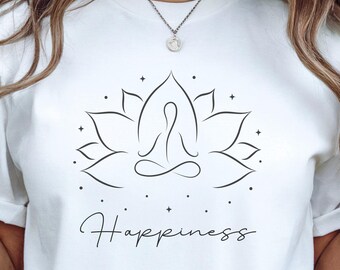 May include: White t-shirt featuring a black line drawing of a person meditating within a lotus flower. The text "Happiness" is written beneath the image.