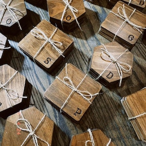 May include: A set of wooden coasters with different letters engraved on them. The coasters are tied together with twine and are arranged on a wooden surface.