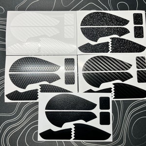 May include: A collection of mouse grip stickers in various designs. The stickers feature patterns like carbon fiber, textured black, and honeycomb. Each sticker set includes pieces for the mouse buttons and sides, all in black and white.