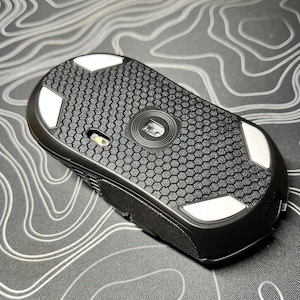 May include: Black computer mouse with a honeycomb pattern on the bottom and white feet.
