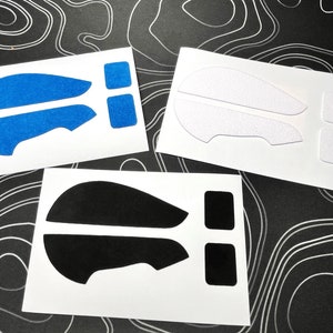 May include: Three sets of mouse grip stickers in blue, white, and black. Each set includes two larger pieces and two smaller square pieces, all on white backing. The blue stickers have a textured, glittery appearance.