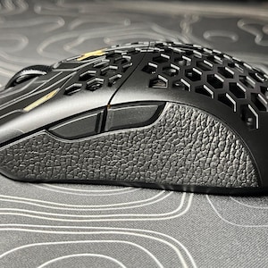 May include: A black gaming mouse with a honeycomb design and a textured grip. The mouse has two side buttons and a gold accent.
