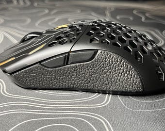 May include: A black gaming mouse with a honeycomb design and a textured grip. The mouse has two side buttons and a gold accent.