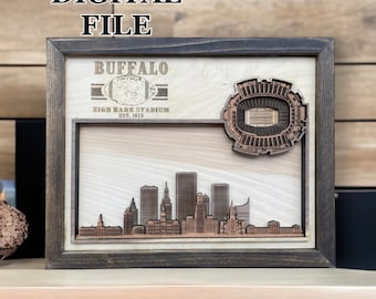 May include: A wooden framed print with a brown wood background. The print features a skyline of Buffalo, New York, with the Highmark Stadium in the upper right corner. The text "Buffalo Highmark Stadium Est. 1973" is printed in gold on a black ribbon.