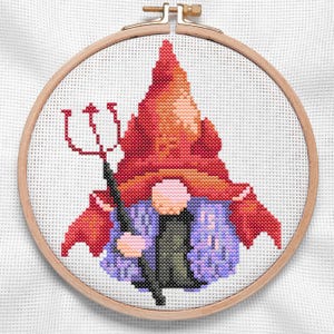 May include: A cross-stitch pattern of a gnome wearing a red hat and a purple jacket, holding a pitchfork. The gnome is surrounded by a wooden embroidery hoop.
