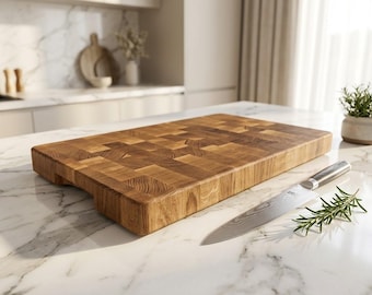Peut inclure: Une planche à découper rectangulaire en bois de bout avec une finition brune naturelle et des motifs de grain de bois visibles, accompagnée d'un couteau de chef en acier inoxydable à manche sombre et d'un brin de romarin frais.