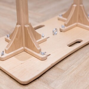 May include: A light-colored wooden base with two wooden supports, each with a triangular base and a central post. Metal hardware secures the supports to the base. The base has two handle cutouts.