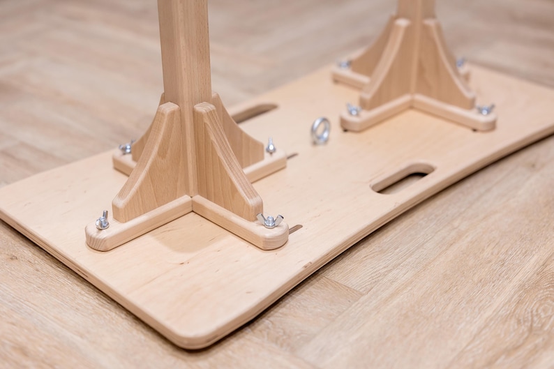 May include: A light-colored wooden base with two wooden supports, each with a triangular base and a central post. Metal hardware secures the supports to the base. The base has two handle cutouts.