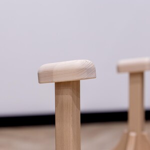 May include: Two wooden handstand blocks with rounded tops and sturdy, vertical supports. The blocks are made of light-colored wood and are designed for balance and stability during handstand practice. The background is a plain white wall.