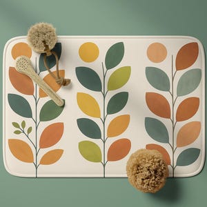 Pode incluir: Tapete de banho retangular com fundo creme e um padrão repetido de folhas estilizadas em laranja, verde e azul. Uma colher de pau e uma esponja natural são colocadas sobre o tapete. O tapete está sobre uma superfície verde.
