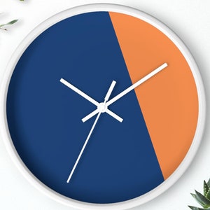 Può includere: Un orologio bianco con un quadrante blu e arancione. L'orologio ha lancette bianche e un bordo bianco.