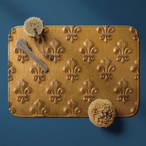 May include: A gold tray with a fleur-de-lis pattern, featuring two natural loofahs and a wooden bath brush.