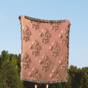 Peut inclure: Une couverture en tissu tissé de couleur or rose avec un motif répétitif de fleurs de lys.