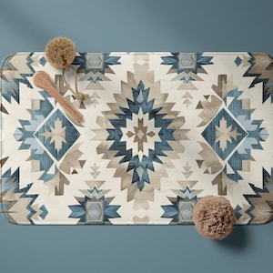 May include: A white bath mat with a blue and brown geometric pattern. The mat has a fringed edge and is made of a soft, absorbent material.