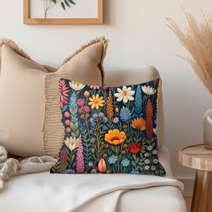 K&ouml;nnte beinhalten: Ein dekoratives Kissen mit einem Blumenmuster. Das Kissen zeigt eine Vielzahl von bunten Blumen, darunter rosa, gelbe, blaue und rote, auf einem dunkelblauen Hintergrund.
