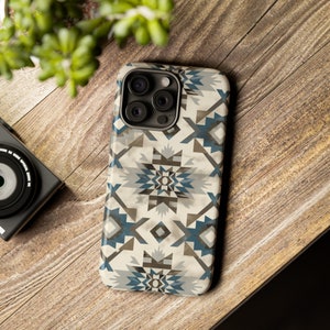 May include: A white phone case with a geometric pattern in shades of blue, brown, and grey. The case has a camera lens cutout with three black camera lenses.