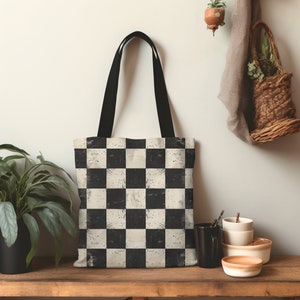 May include: A black and white checkered tote bag with a distressed look. The bag has black handles and is made of canvas.