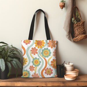 May include: White tote bag with a colorful floral pattern in orange, yellow, pink, and teal. The design features wavy lines and black handles. The bag is made of a durable fabric and is suitable for carrying groceries or personal items.