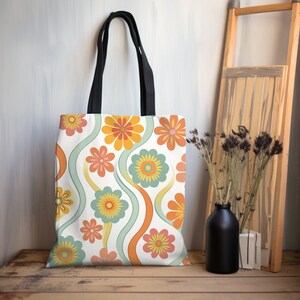 May include: A white tote bag with a retro floral pattern in orange, yellow, and teal. The bag has black handles and is displayed on a wooden surface. The floral design features wavy lines and various flower shapes.