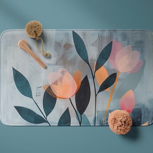 May include: A light blue bath mat with a floral design featuring pink and orange flowers and green leaves. The mat is on a blue background with two bath accessories.