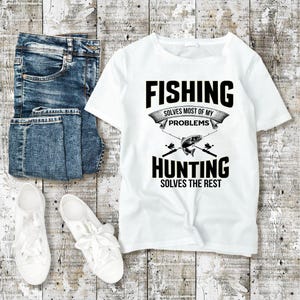 以下が含まれることがあります： 黒い文字で「釣りは私のほとんどの問題を解決する。狩猟は残りを解決する。」と書かれた白いTシャツ。テキストは黒いリボンで囲まれています。テキストの下には、魚と釣り竿の白黒のイラストがあります。