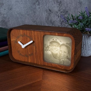 Peut inclure: Une horloge en bois avec un cadre photo. L'horloge a un cadran clair avec des aiguilles blanches et le texte "Where are my forever? The future days". Le cadre photo affiche une image en noir et blanc d'un couple. L'horloge est sur une surface en bois.