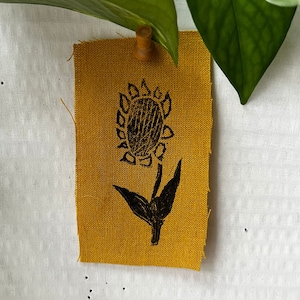 May include: A yellow fabric patch with a black silhouette of a sunflower printed on it.