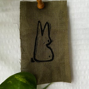 Könnte beinhalten: Ein brauner Stoff-Patch mit einer schwarzen, handgezeichneten Silhouette eines Kaninchens.