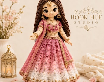 May include: A crochet doll with long brown hair wearing a pink and white ombre lehenga with gold embroidery. The doll features large dark eyes, gold earrings, a necklace, and a maang tikka. The text HOOK HUE STUDIO is visible in the upper right.