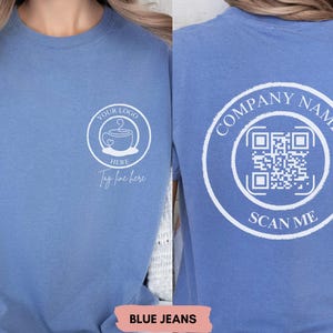 May include: A blue denim t-shirt with a white design on the front. The design includes a coffee cup with a heart and the text "Your Logo Here" and "Tag line here". The back of the shirt has a white circle with the text "Company Name" and a QR code with the text "Scan Me".