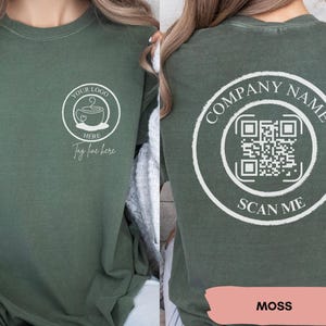 May include: A green long-sleeved t-shirt with a white design on the front that says "Your Logo Here" and a coffee cup with a heart. The back of the shirt has a white circle with the text "Company Name" and a QR code with the text "Scan Me". The shirt is labelled "Moss".