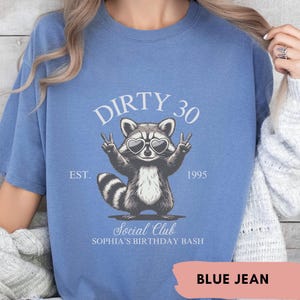 May include: A blue jean t-shirt with a raccoon wearing sunglasses and peace signs. The shirt says "Dirty 30 Est. 1995 Social Club Sophia's Birthday Bash".