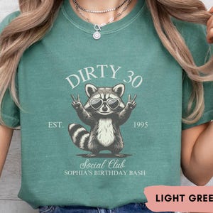 May include: Light green t-shirt with a raccoon wearing sunglasses and the text "Dirty 30 Est. 1995 Social Club Sophia's Birthday Bash"