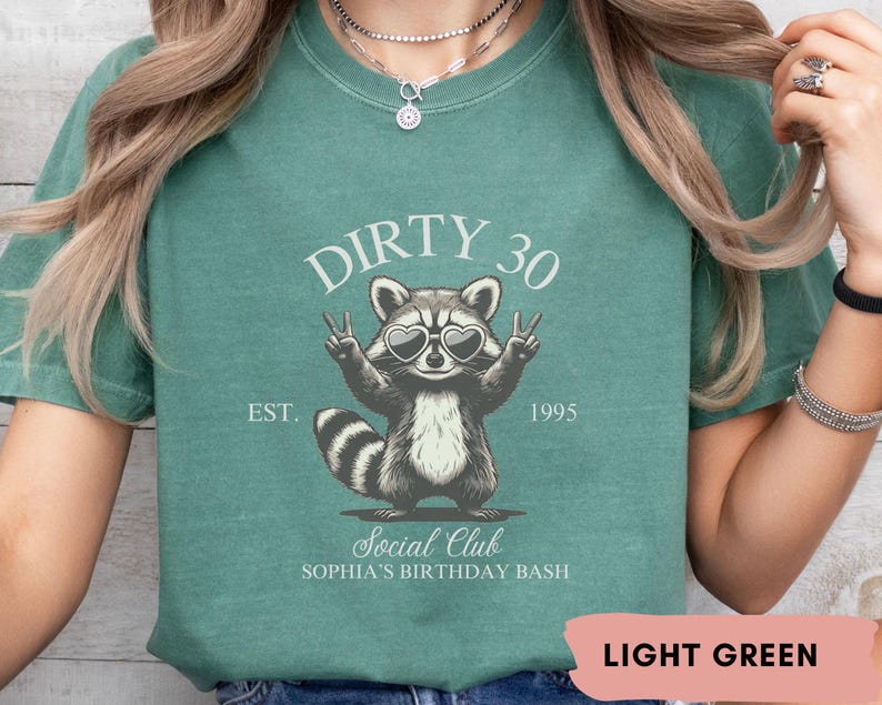May include: Light green t-shirt with a raccoon wearing sunglasses and the text "Dirty 30 Est. 1995 Social Club Sophia's Birthday Bash"