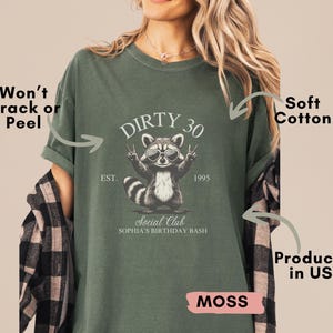 May include: A moss green t-shirt with a raccoon graphic and the text "Dirty 30 Social Club Sophia's Birthday Bash" printed on the front. The shirt is made of soft cotton and is produced in the USA.