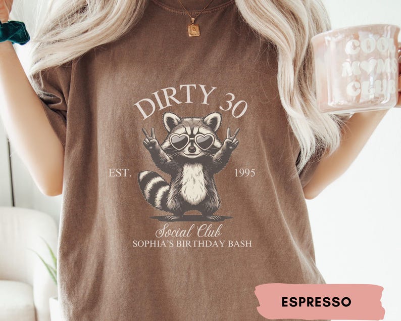 May include: A brown t-shirt with a raccoon wearing sunglasses and the text "Dirty 30 Est. 1995 Social Club Sophia's Birthday Bash" printed on it. The shirt is labeled "Espresso".