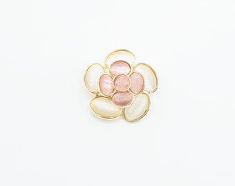 May include: A flower-shaped brooch with a gold-tone metal frame. The brooch features pink and off-white oval-shaped stones arranged in a floral pattern. The centre stones are a darker pink, and the outer stones are a lighter, pearlescent white.