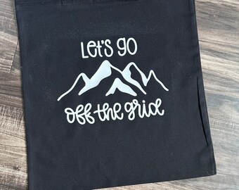 Peut inclure: Sac fourre-tout en toile noire avec du texte blanc qui dit "Let's go off the grid" et un graphique de montagnes.