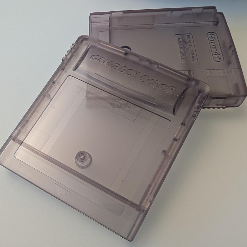 May include: Two translucent gray Game Boy Color cartridges. The text "GAME BOY COLOR" is visible on one cartridge. The cartridges are made of plastic and have a rectangular shape. The Nintendo logo is visible on the top cartridge.