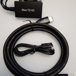 May include: A black Xbox to HD converter with a black HDMI cable, a black USB cable, and a black cable with a connector for an older console.