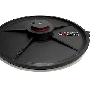 以下が含まれることがあります： 赤と白の中心と5本の腕を持つ、黒色の円形の3Dプリントディスク。ディスクには「CANE RIVER GOLOW」という文字が印刷されています。