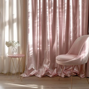 May include: A pink velvet chair with gold legs sits next to a gold metal side table with a pink top. The chair and table are in front of a pink velvet curtain.