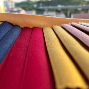 May include: A close-up of a fabric swatch book with a variety of colors, including navy blue, burgundy, gold, and purple.