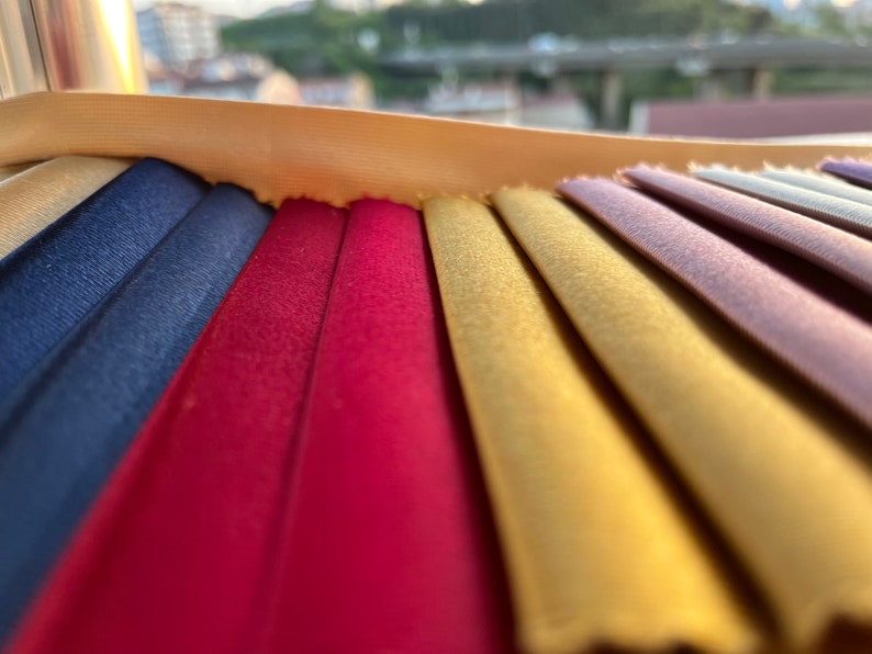 May include: A close-up of a fabric swatch book with a variety of colors, including navy blue, burgundy, gold, and purple.