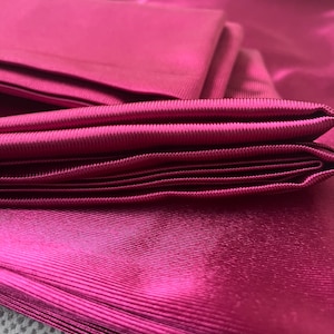May include: A stack of deep pink satin fabric with a ribbed texture. The fabric is folded neatly and has a soft, luxurious feel.