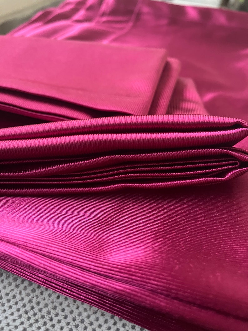 May include: A stack of deep pink satin fabric with a ribbed texture. The fabric is folded neatly and has a soft, luxurious feel.