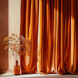May include: A vase with a dried flower arrangement in front of a set of orange velvet curtains.