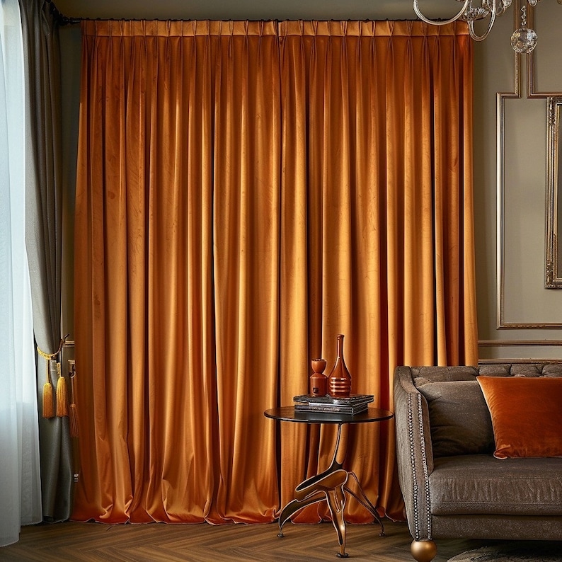 May include: A pair of orange velvet curtains hang in a living room with a brown leather sofa and a small side table with a vase and books.